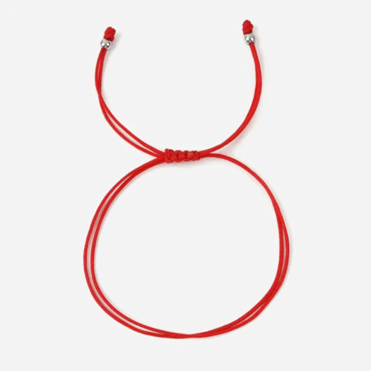 Photo d'un bracelet cordon rouge fermé par un noeud avec 2 perles dorées au bout.