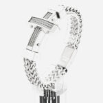 Bracelet en maille épaisse argenté avec une croix chrétienne dessus, posé sur un support transparent.