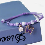 Bracelet tressé pendentif papillon pour petite fille posé sur un livre.