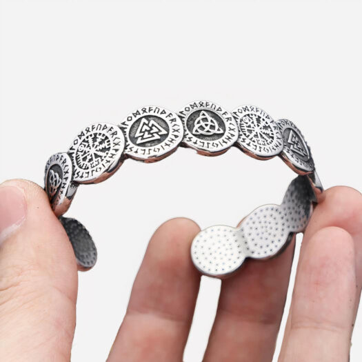 Bracelet gris en métal avec des pièces gravées et collées les unes aux autres. Il est tenu par une main