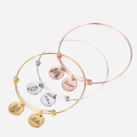 Photo de trois bracelet jonc avec des breloques gravées, un bracelet doré, un argenté et un rose, superposés.