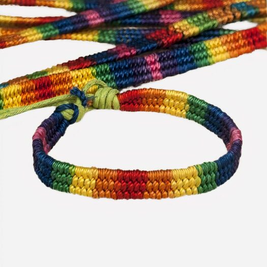 Un bracelet brésilien aux couleurs de l'arc en ciel LGBT fermé par un noeud et posé sur une toile de jute. Plusieurs bracelets sont en arrière plan