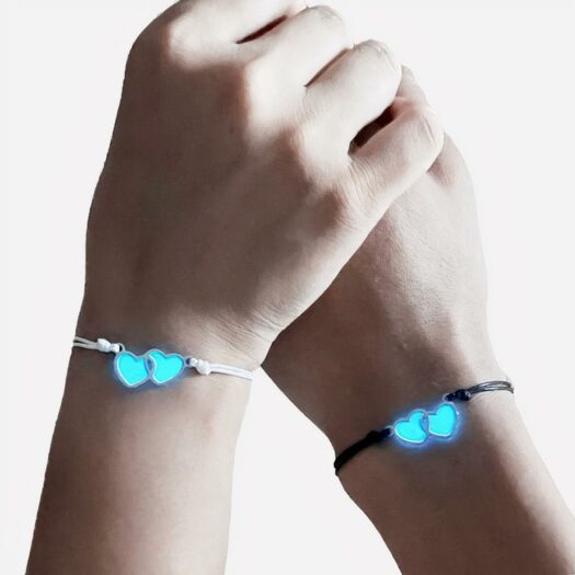 Deux mains qui portent un bracelet cordon, un noir et l'autre blanc, ornés de cœurs fluorescents.