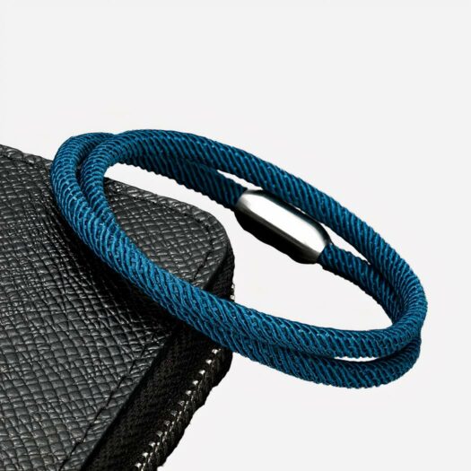 Un bracelet cordon bleu avec une finition argentée est posé sur une pochette noire