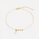 Photo d'un bracelet de cheville en or jaune pour femme avec coeur en pendentif et trois perles rondes à facettes, le tout sur un fond blanc