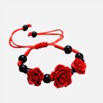 Un bracelet rouge avec des perles noires et 3 roses rouges posé sur une table