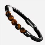 Photo d'un bracelet tressé noir orné de cinq perles en pierre oeil de tigre rouge et fermeture aimant, sur un fond gris foncé