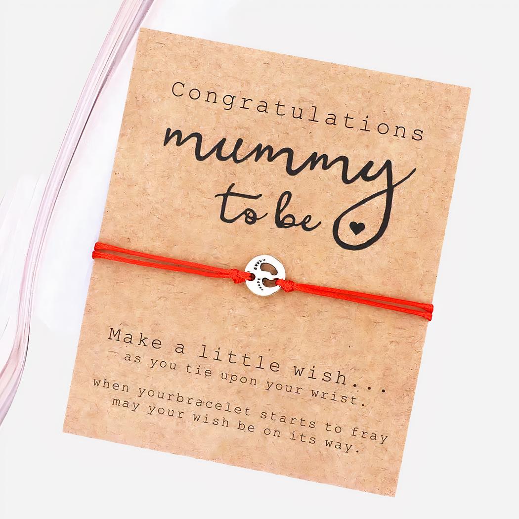 Bracelet porte-bonheur pour future maman On voit un bracelet avec un cordon rouge et une médaille qui montre des empreintes de pied de bébé.