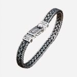 Photo d'un bracelet pour homme en argent certifié sterling 925, fermoir à poussoir travaillé, et mailles entrelacées, posé sur un rondin de bois