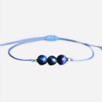 Photo d'un bracelet oeil de tigre enfant en cordon de coton réglable avec trois perles bleues sur un fond gris