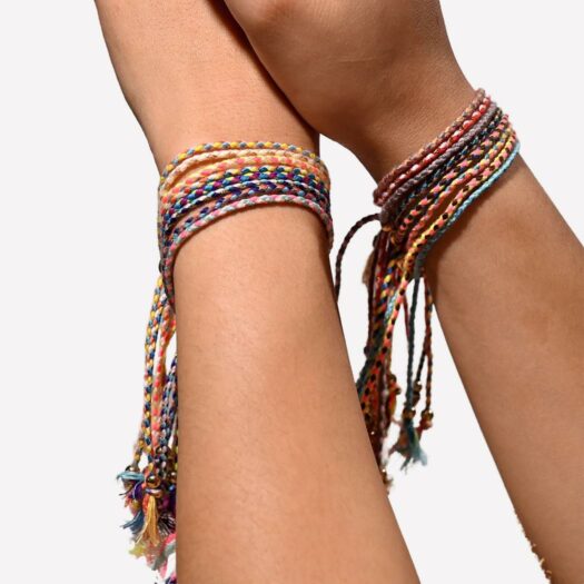 2 avant bras avec plusieurs bracelet multicolores à chaque poignet. La photo est prise d'une plage