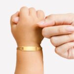 Une main d'enfant portant une gourmette dorée entoure le doigt d'une main d'adulte