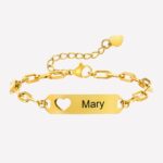 Une gourmette dorée avec des maillons larges, une plaque où est écrit Mary et où est inscrusté un coeur ajouré. Présence au niveau du fermoir d'une petite chaine avec un coeur au bout