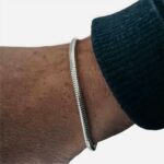 Un poignet d'homme porte un bracelet argenté. Le bas d'une manche bleue marine apparait