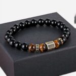 Un bracelet avec des perles noires, des perles marron, 2 petites pièces et une grande pièce centrale en métal